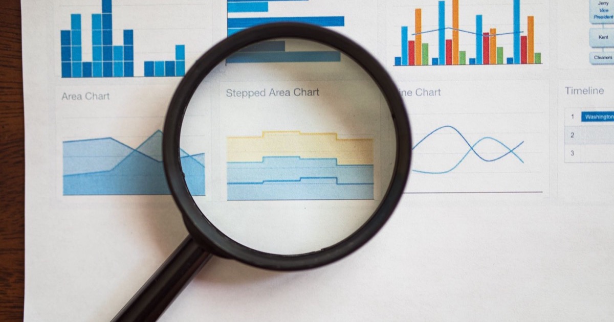 A magnifying glass held over printed charts and graphs